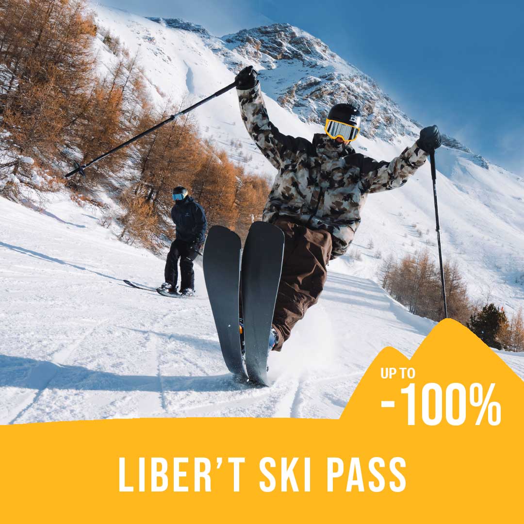 2 skiers on a slope with larch trees and snowy moutains in the background